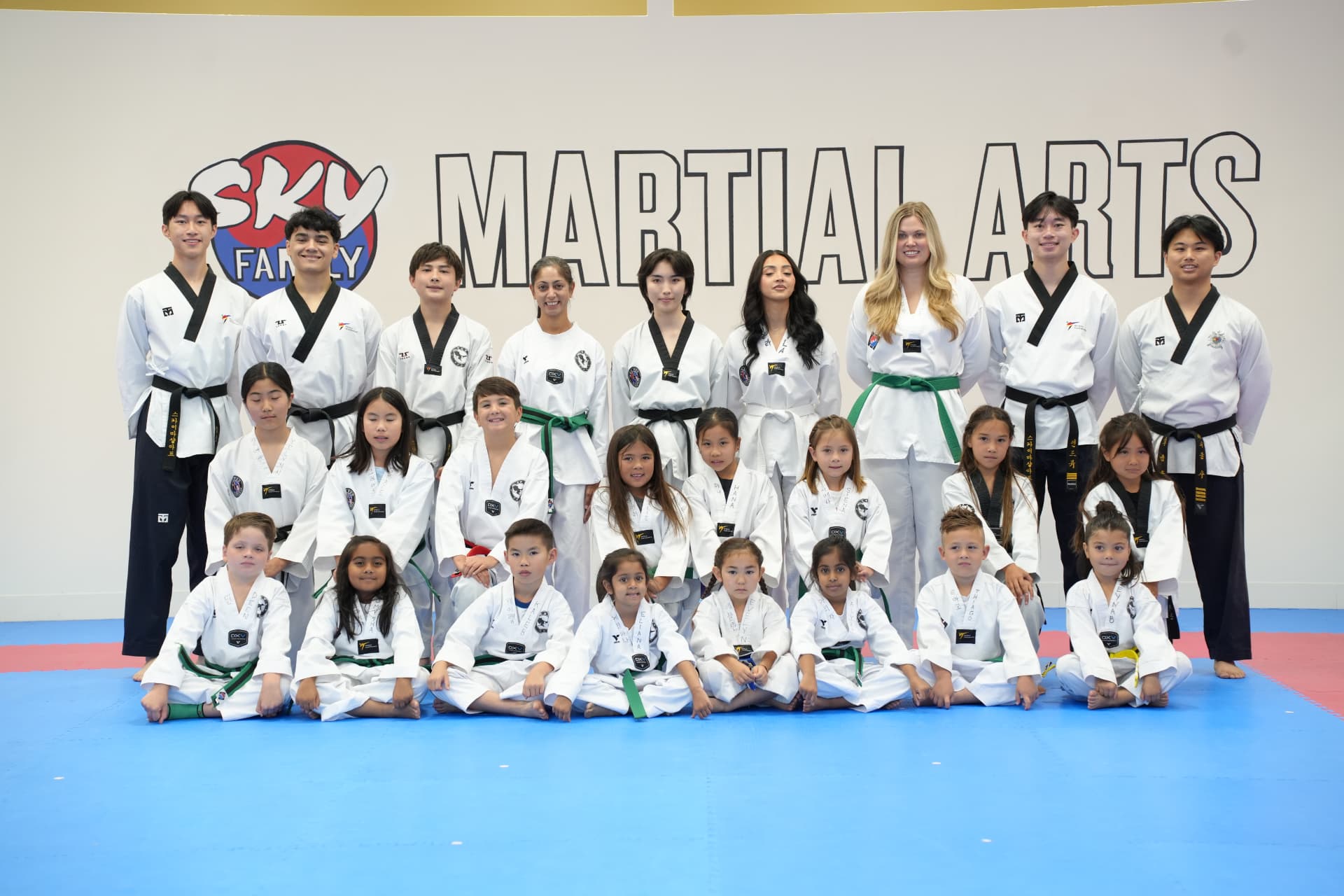 Sky Family Martial Arts students and instructors posed in front of the SKY Martial Arts wall